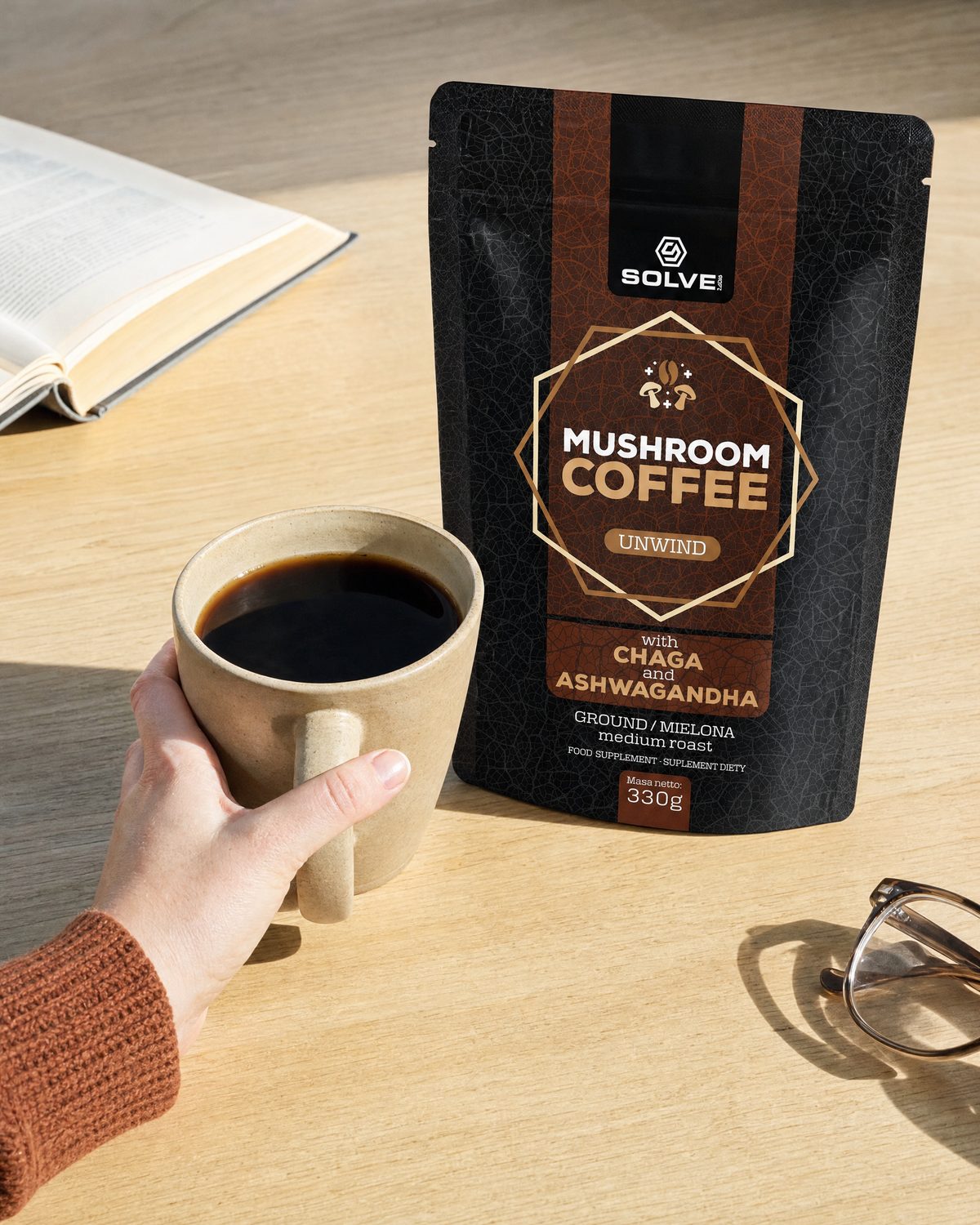 A hand lifting a stoneware cup of coffee beside a bag of Mushroom Coffee with Chaga