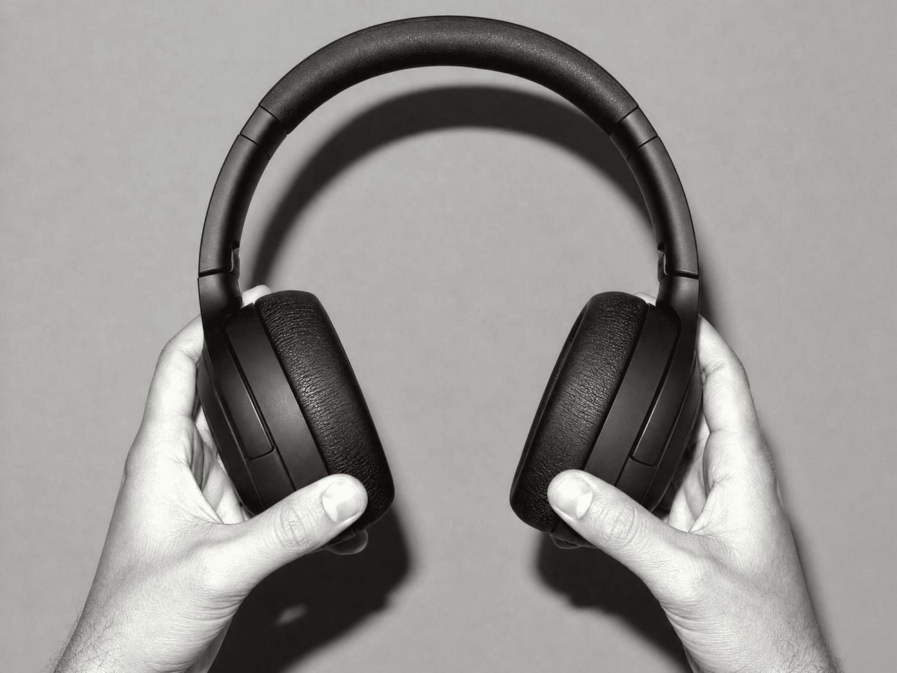Two hands holding a pair of over-ear headphones, in black and white