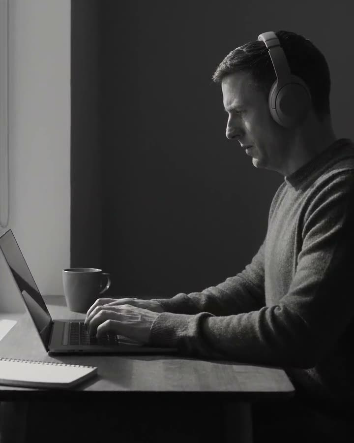 A man at a desk with headphones on, working on a laptop, phone nowhere in sight