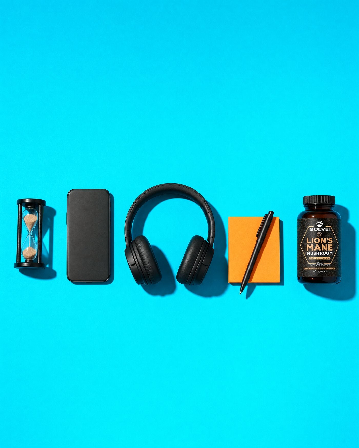 Five things in a row on a cyan ground, seen from above: an hourglass, a phone face down, headphones, a pad of sticky notes with a pen, and the Solve Labs Lion's Mane jar