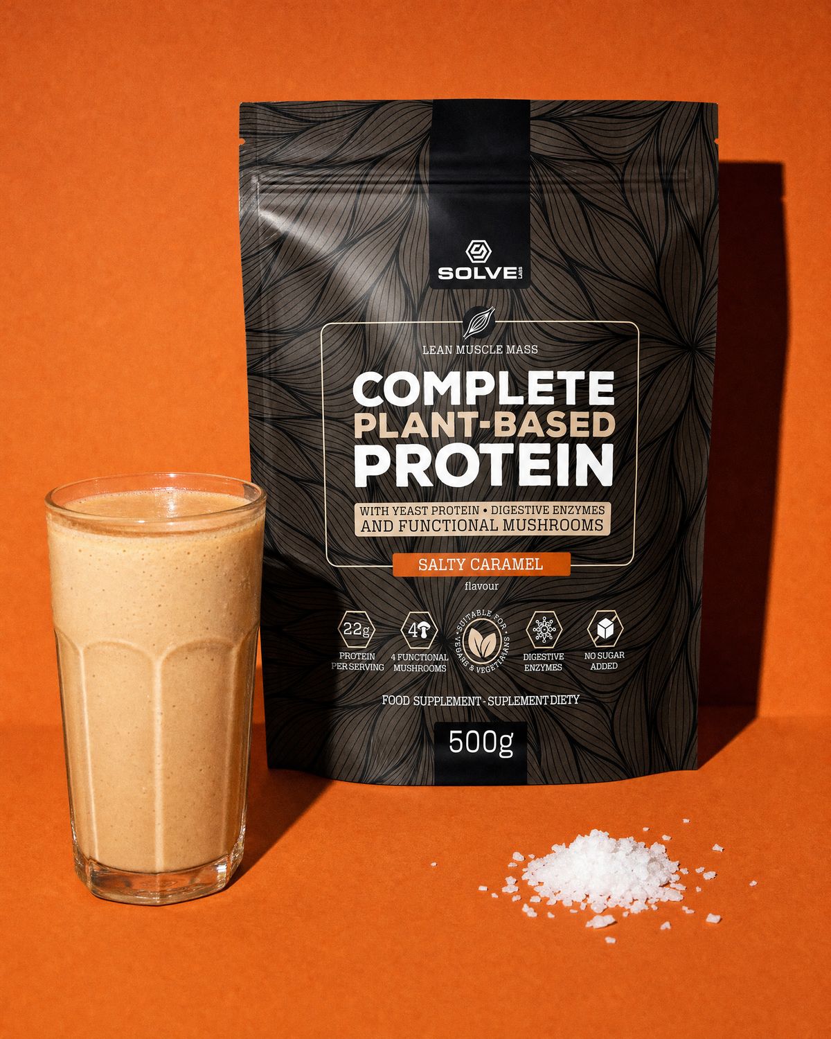 The salted caramel pouch of Solve Labs plant protein on a terracotta backdrop with a glass of shake