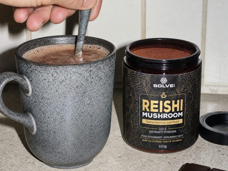 A mug of cacao being stirred beside a jar of Reishi powder and a bar of dark chocolate