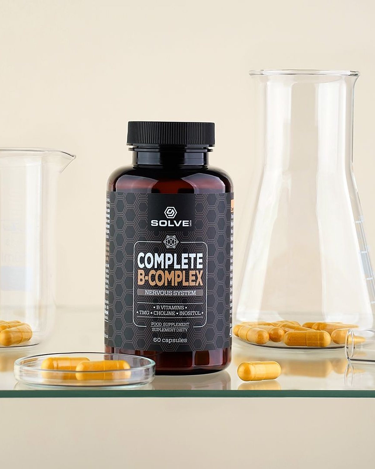 The jar of Solve Labs Complete B-Complex on a glass shelf between a beaker and a flask, yellow capsules in a dish