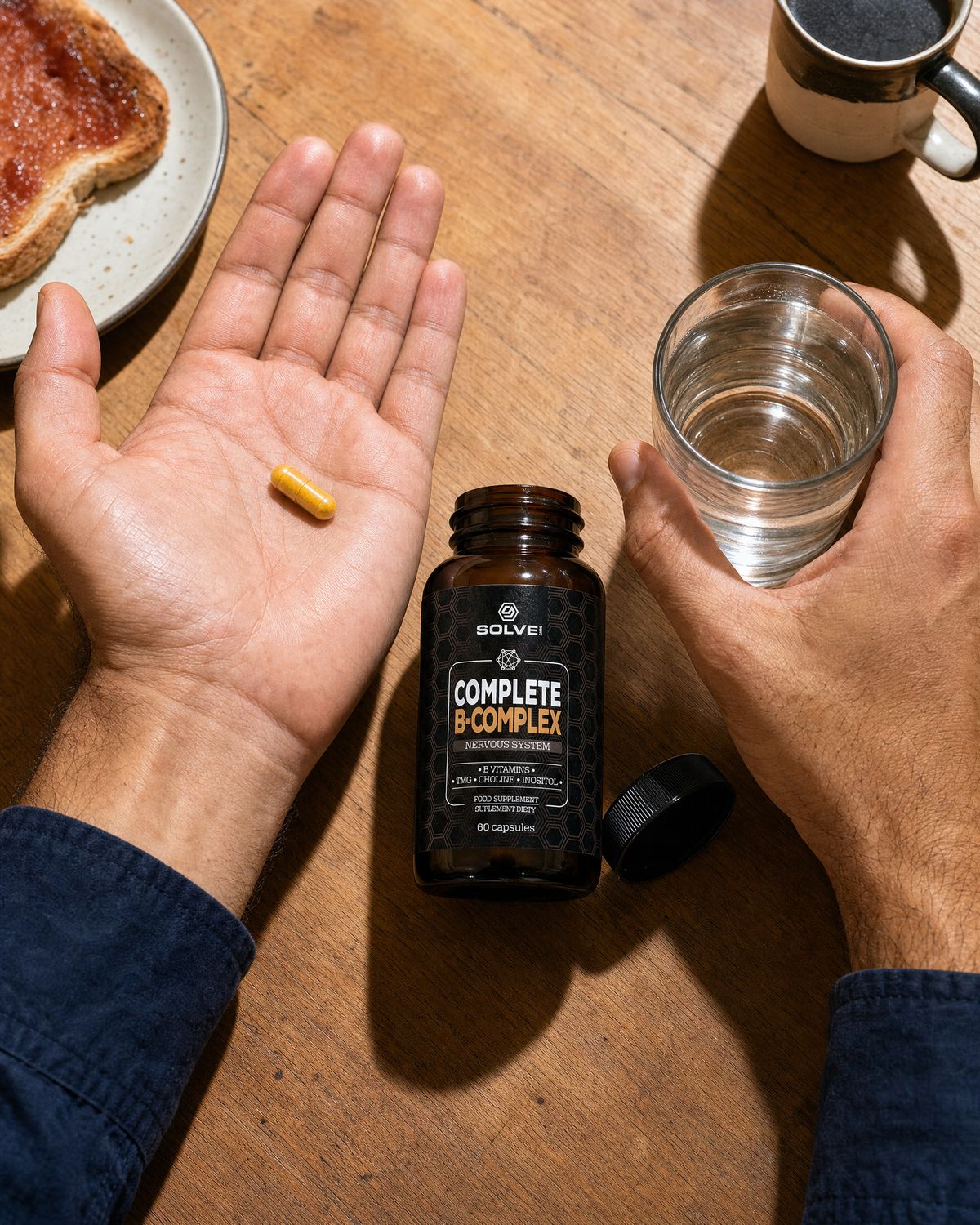 One yellow B-Complex capsule in an open palm beside a glass of water and the open jar