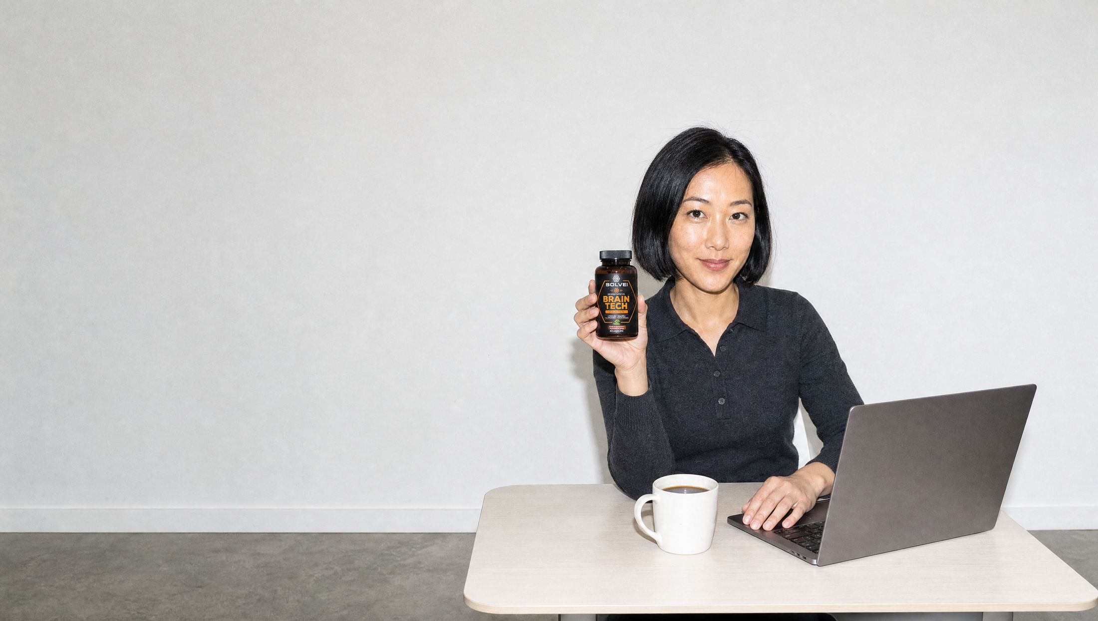 A woman at a desk in a bright studio office, holding up the jar of Solve Labs Brain Tech
