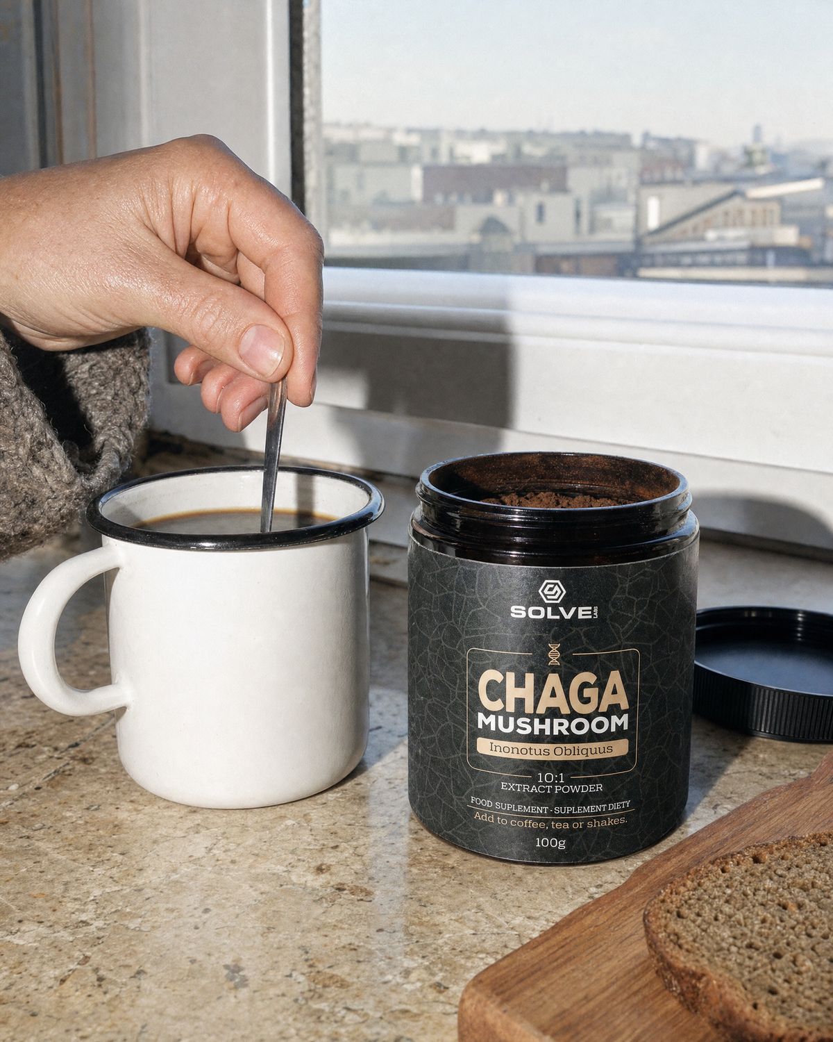 A hand stirring an enamel mug of coffee by a window beside the open jar of Solve Labs Chaga