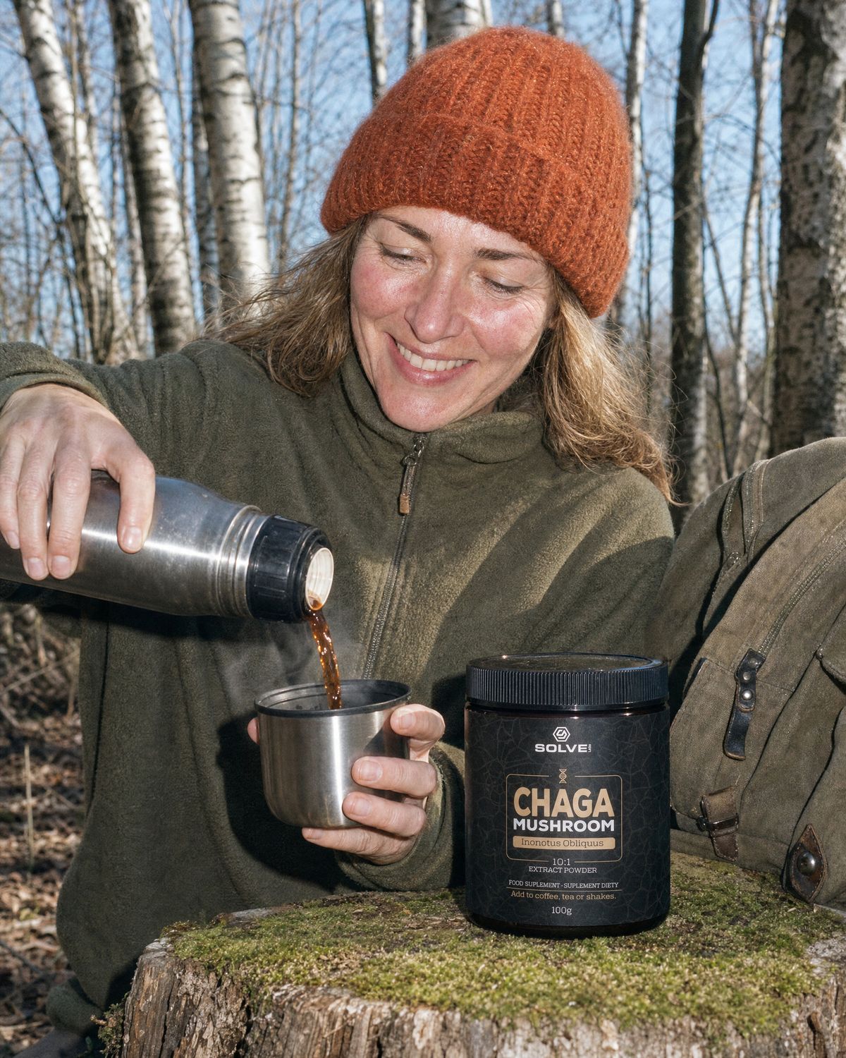 Hands pouring coffee from a flask among birch trees, the jar of Solve Labs Chaga on a tree stump