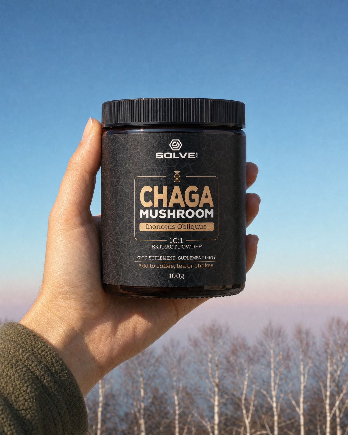 A hand holding up a jar of Solve Labs Chaga powder against a cold morning sky over birch trees