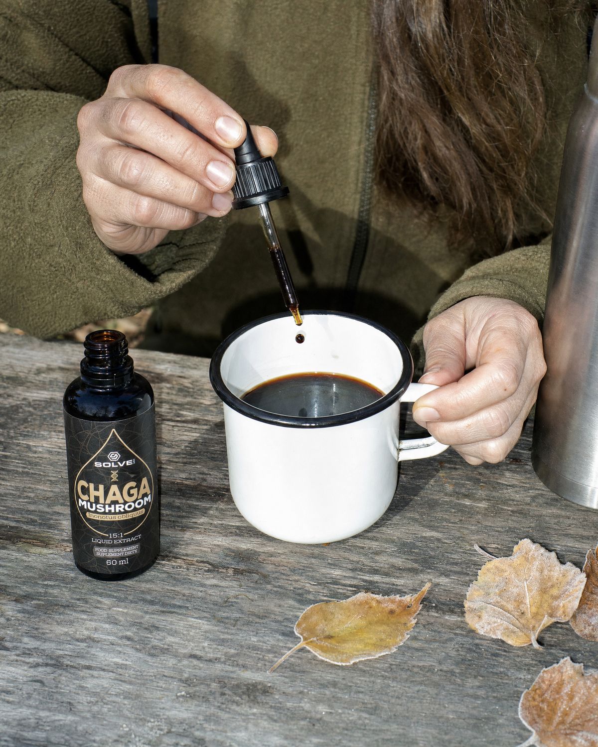 A dropper of chaga liquid extract over an enamel mug of coffee beside the open bottle