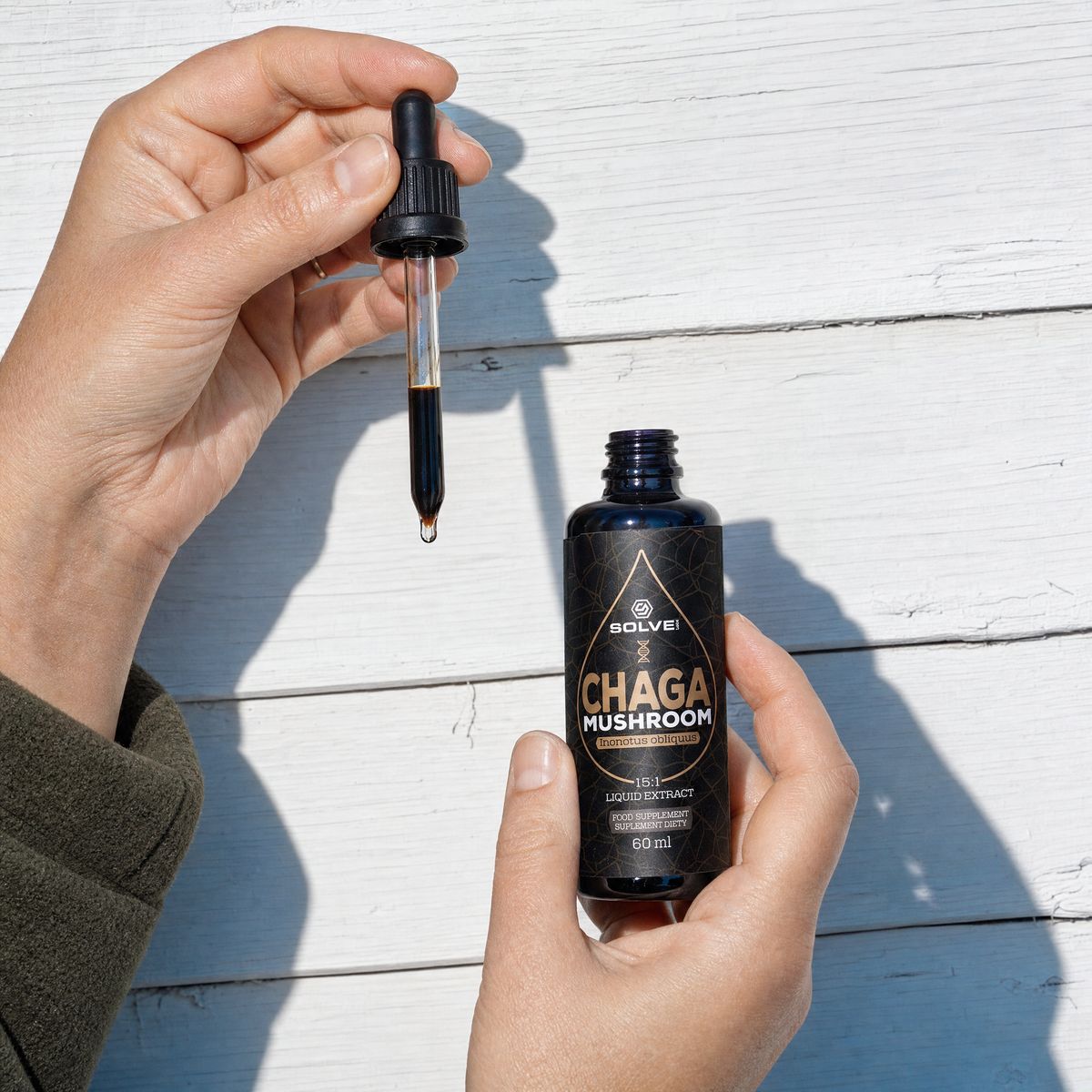 A hand holding a full dropper above the open bottle of chaga drops