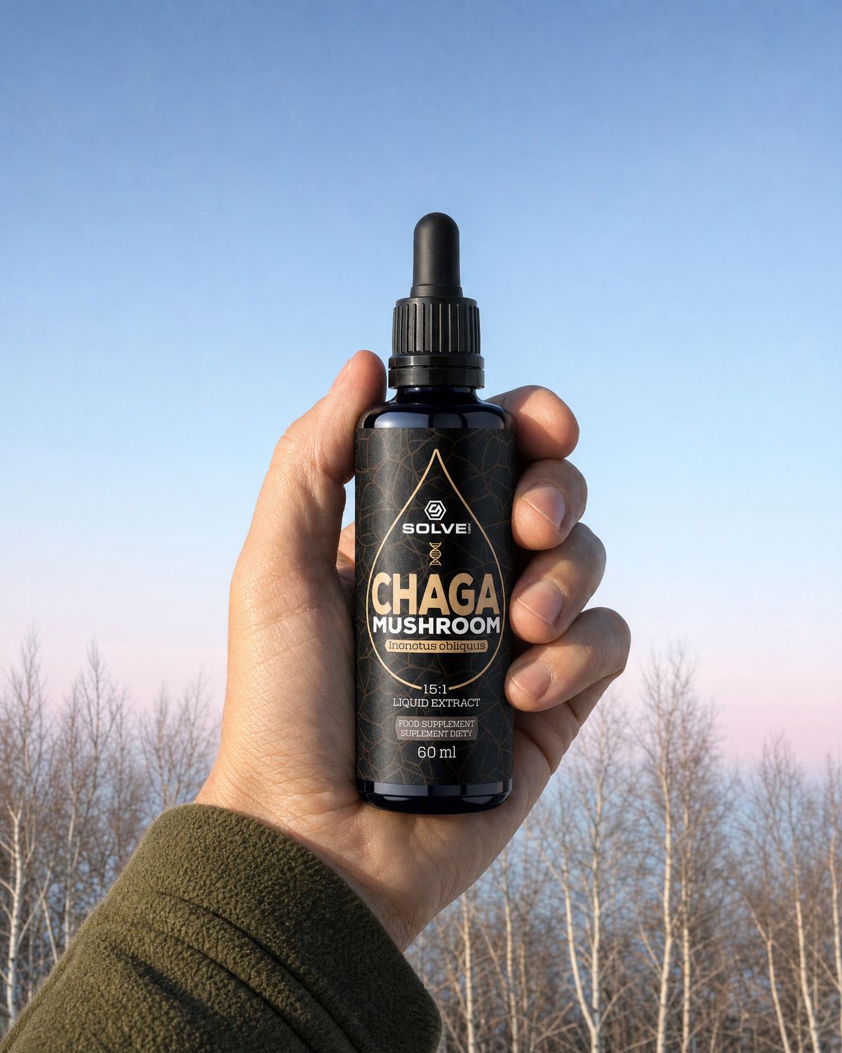 A hand holding up a bottle of Solve Labs Chaga drops against a cold morning sky over birch trees