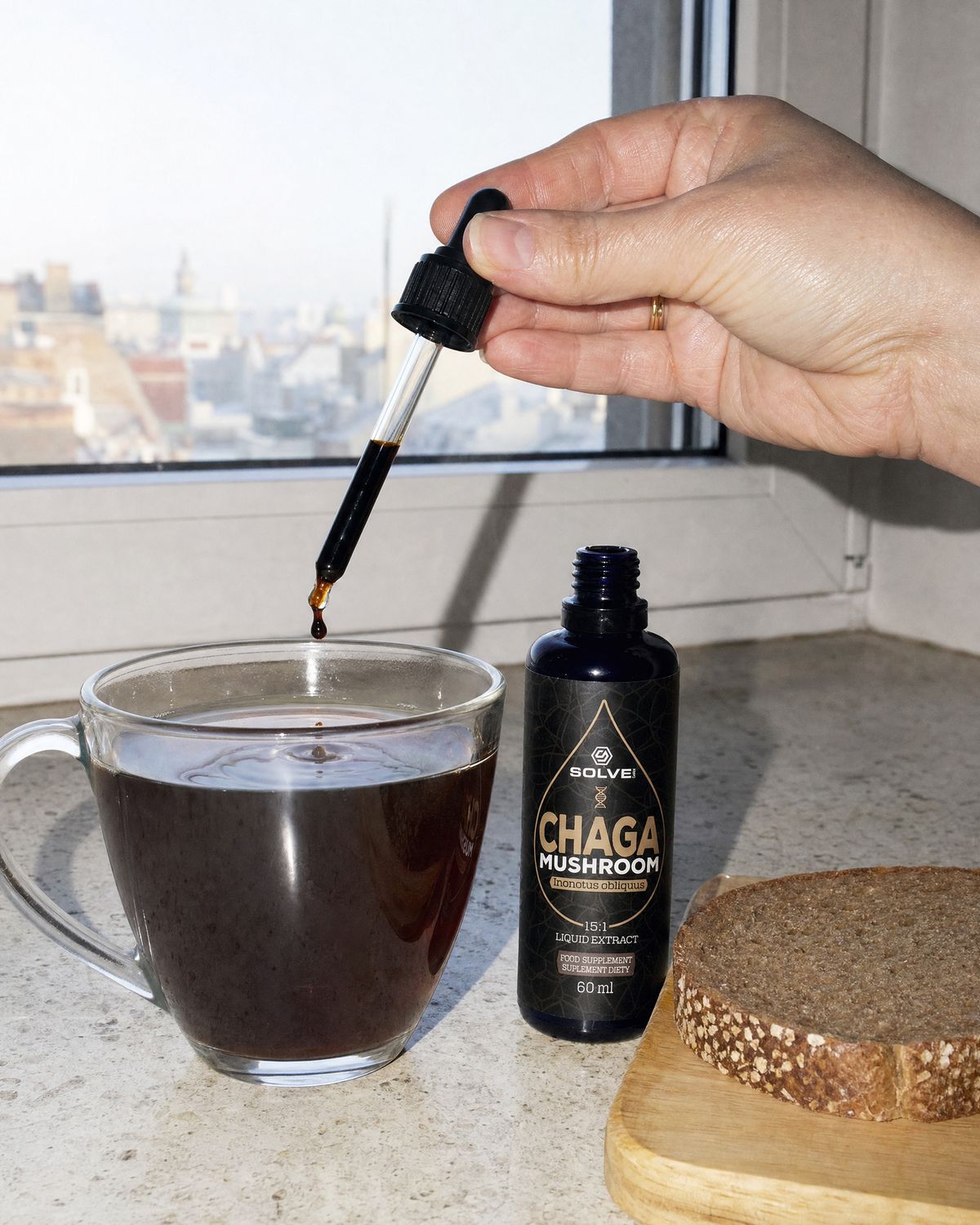 A dropper of chaga liquid extract over a glass of tea by a window beside the bottle