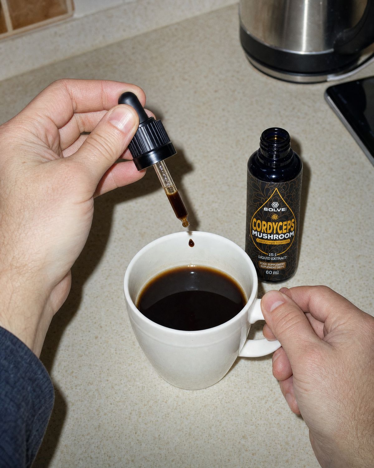 A dropper of cordyceps liquid extract over a mug of coffee beside the open bottle