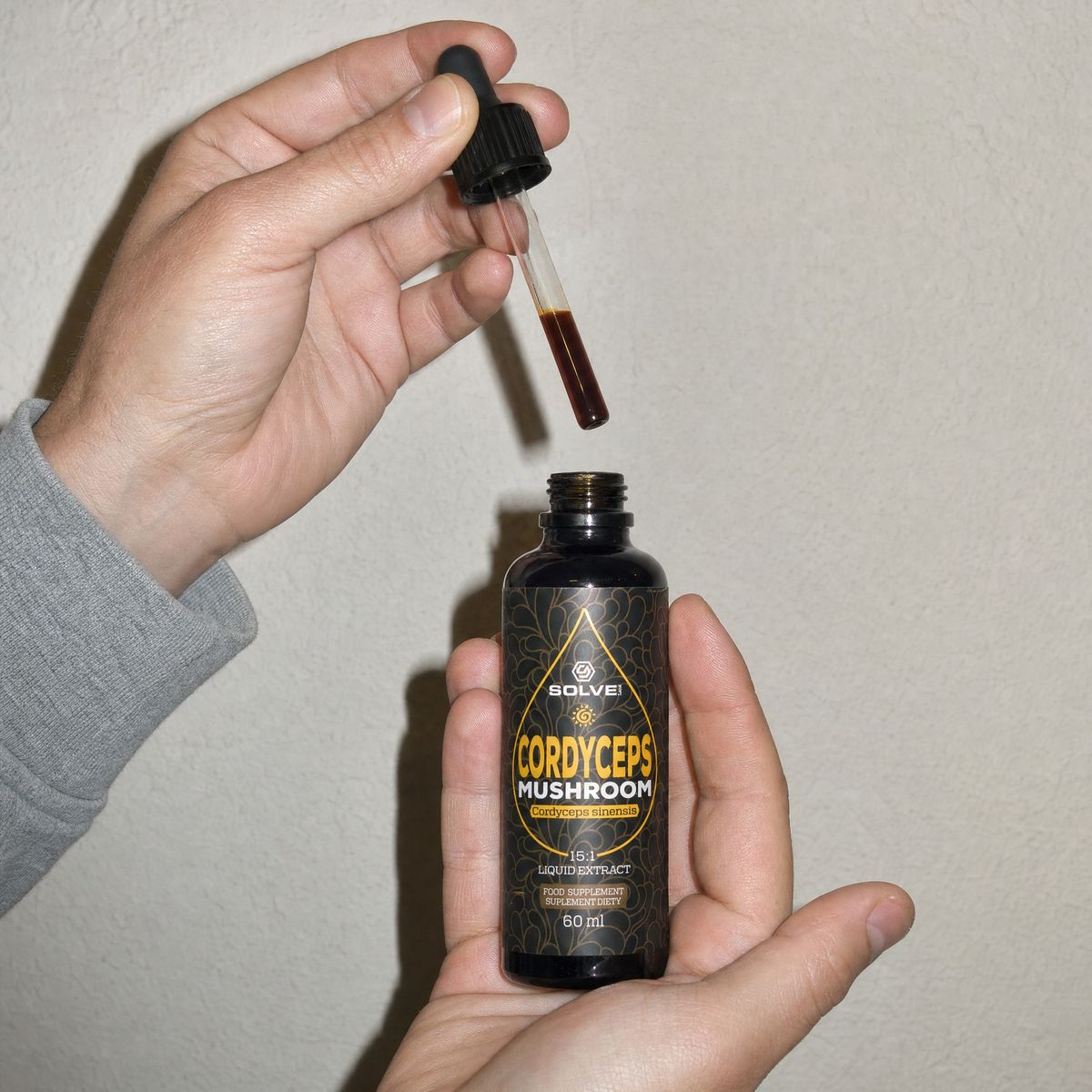 A hand holding a full dropper above the open bottle of cordyceps drops