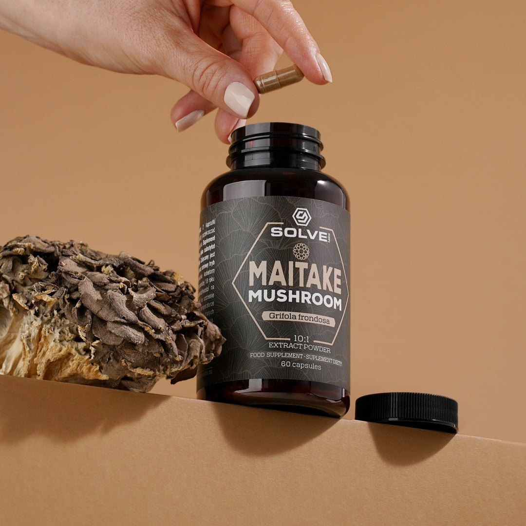 Una mano deja caer una cápsula en el bote abierto de Solve Labs Maitake, con un maitake entero al lado