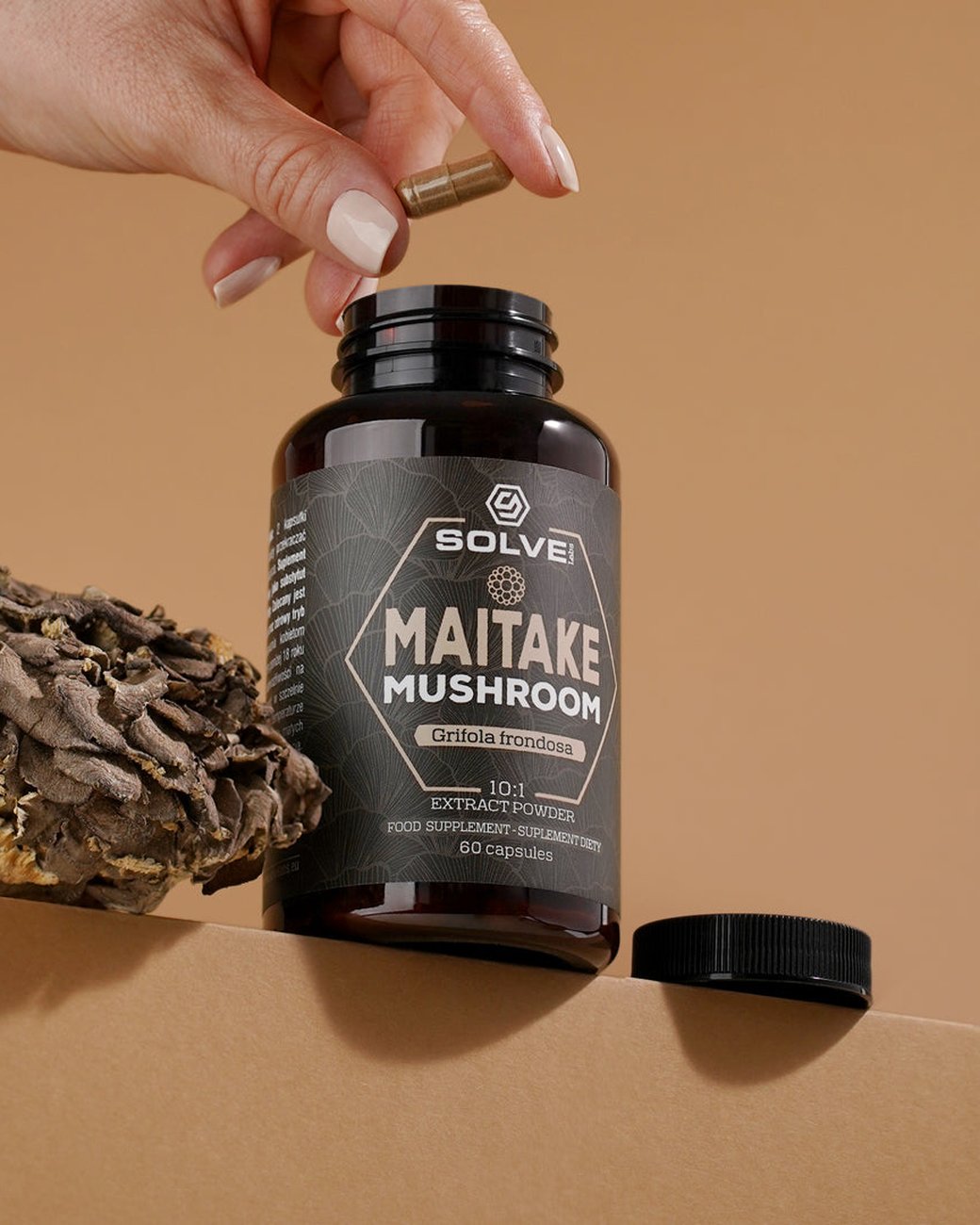 Una mano deja caer una cápsula en el bote abierto de Solve Labs Maitake, con un maitake entero al lado