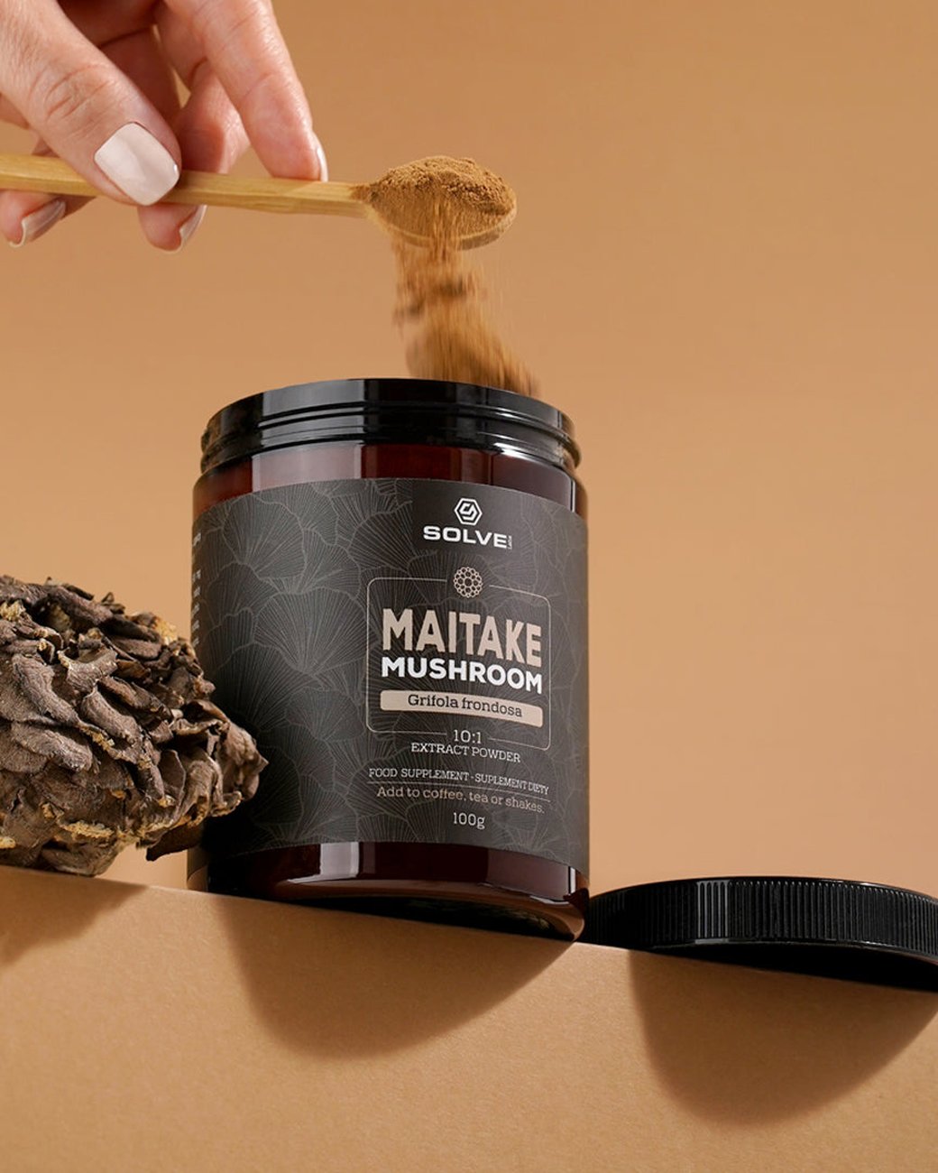 Eine Hand gibt einen Holz-Messlöffel Maitake-Pulver in die offene Dose Solve Labs Maitake