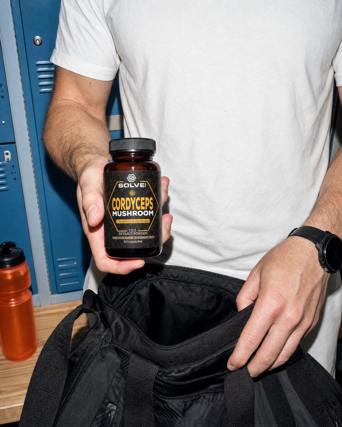 A hand dropping a jar of Solve Labs Cordyceps capsules into a sports bag in front of gym lockers
