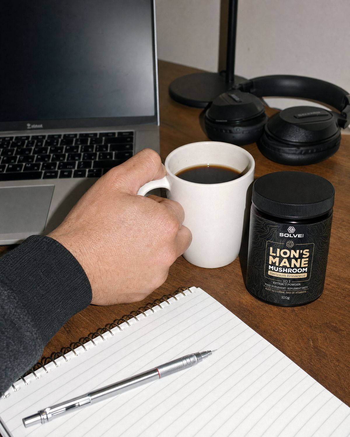 A working desk with a laptop, a notebook, a mug of coffee and the jar of Solve Labs Lion&rsquo;s Mane