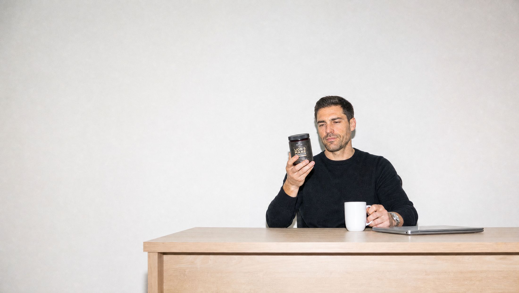 A man at his desk reading the back label of a jar of Solve Labs Lion&rsquo;s Mane powder