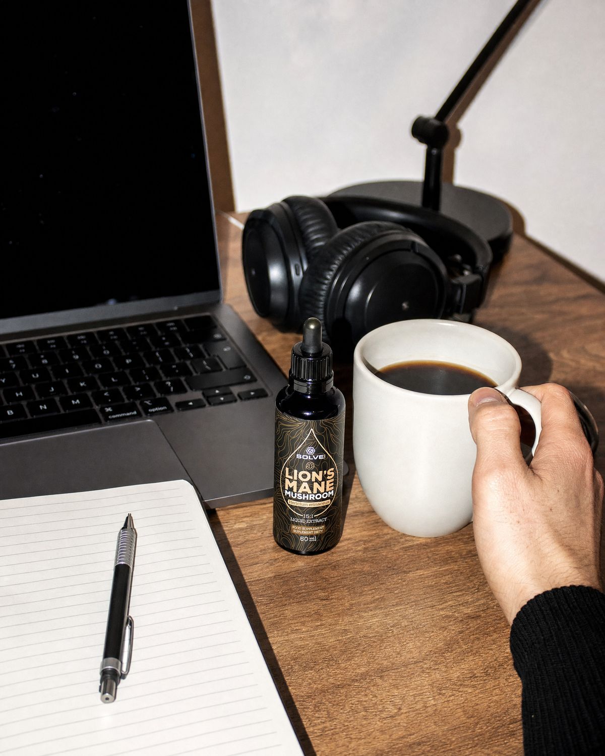 A working desk with a laptop, a notebook, a mug of coffee and the bottle of Solve Labs Lion&rsquo;s Mane drops