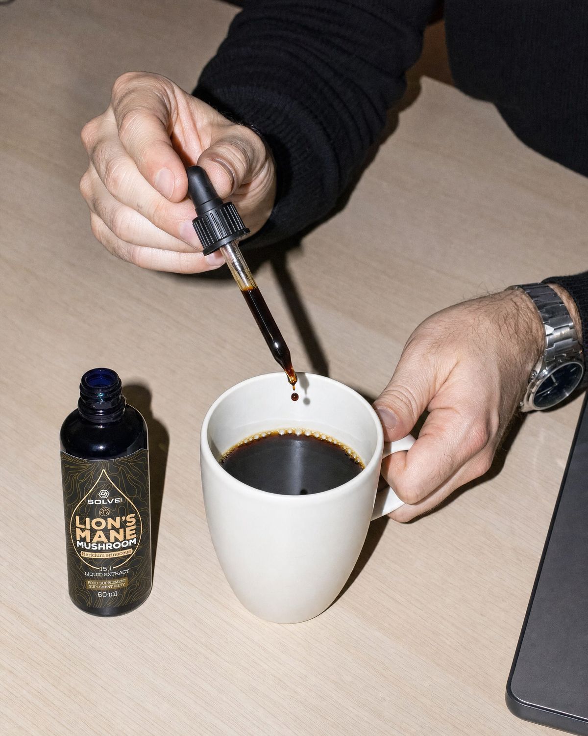 A dropper of lion&rsquo;s mane liquid extract over a mug of coffee on a desk beside the open bottle