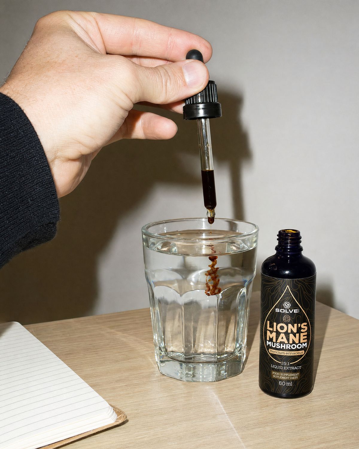 A dropper of lion&rsquo;s mane liquid extract over a glass of water on a desk beside the bottle