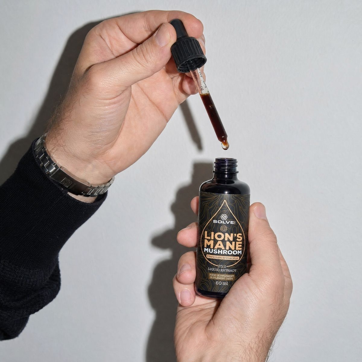 A hand holding a full dropper above the open bottle of lion&rsquo;s mane drops