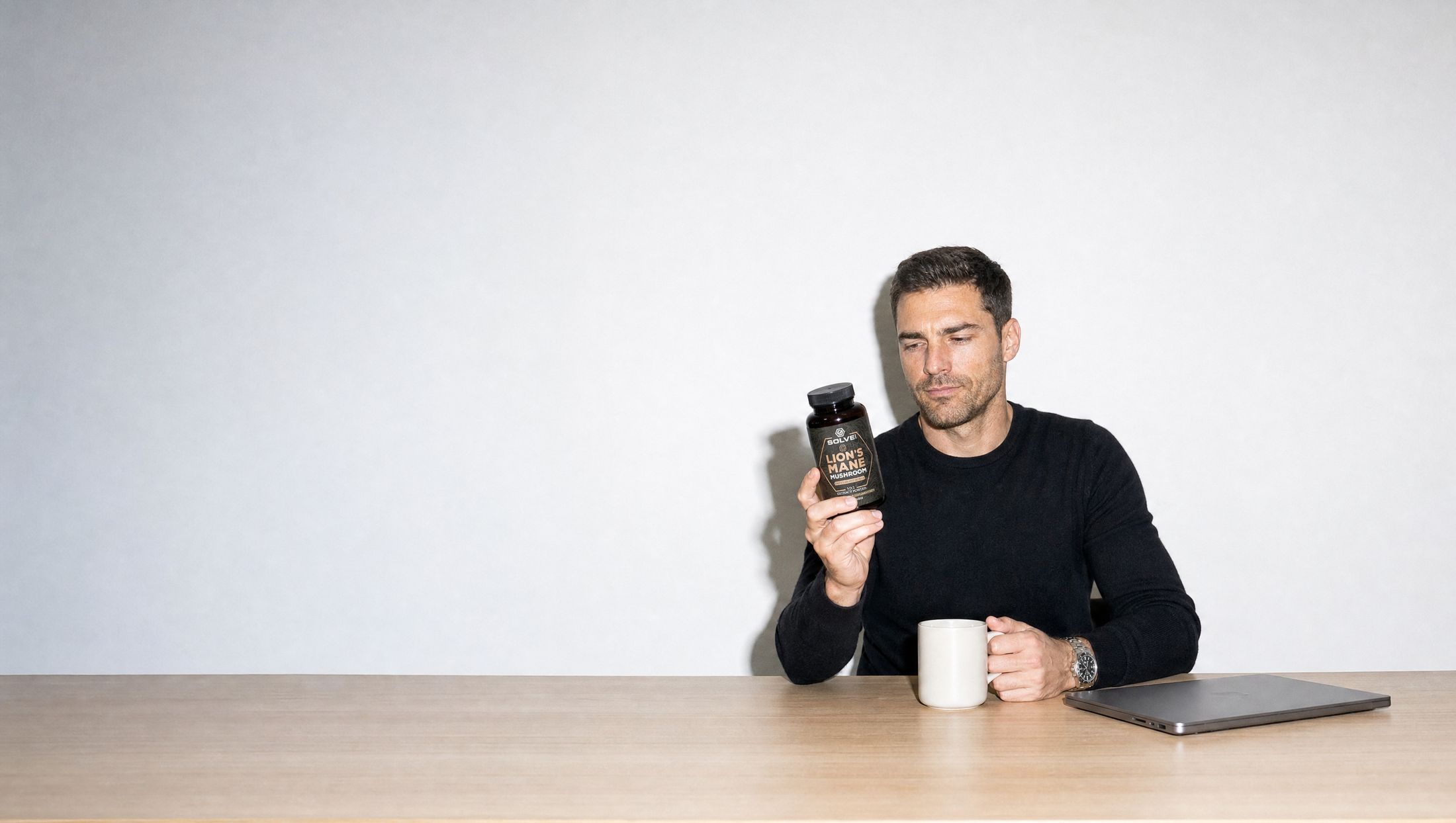 A man at his desk reading the back label of a jar of Solve Labs Lion&rsquo;s Mane capsules