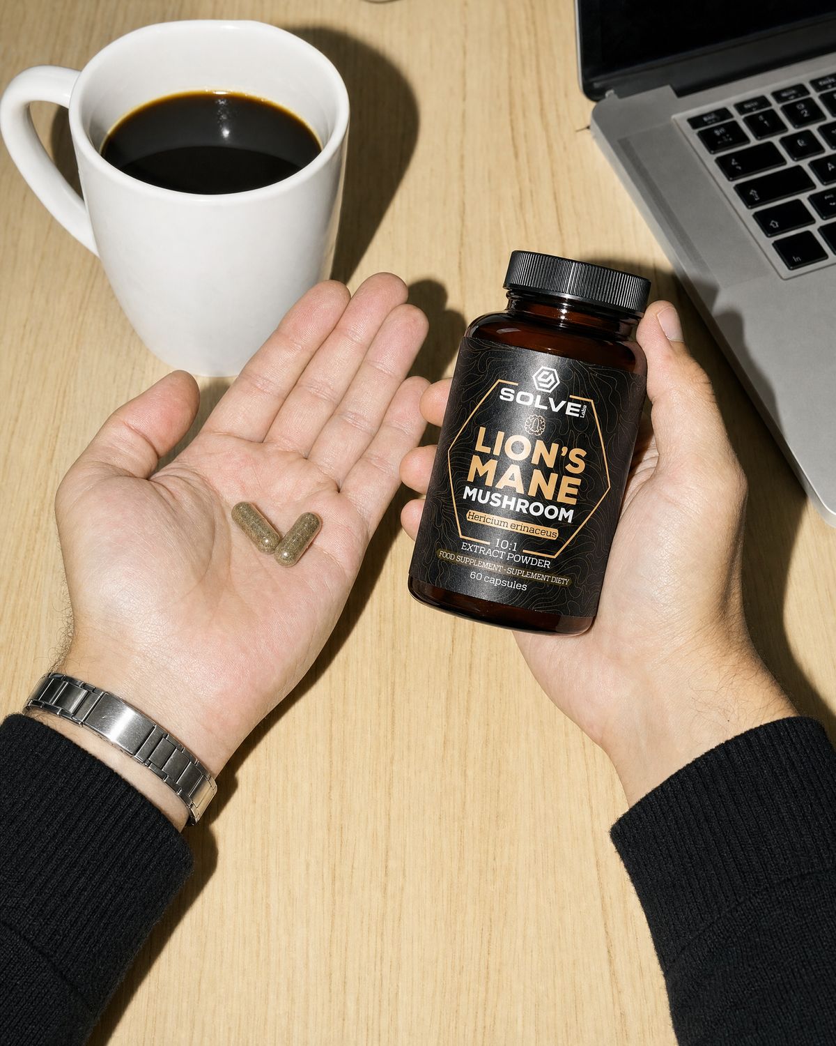 Two lion&rsquo;s mane capsules in an open palm beside the jar and a mug of coffee