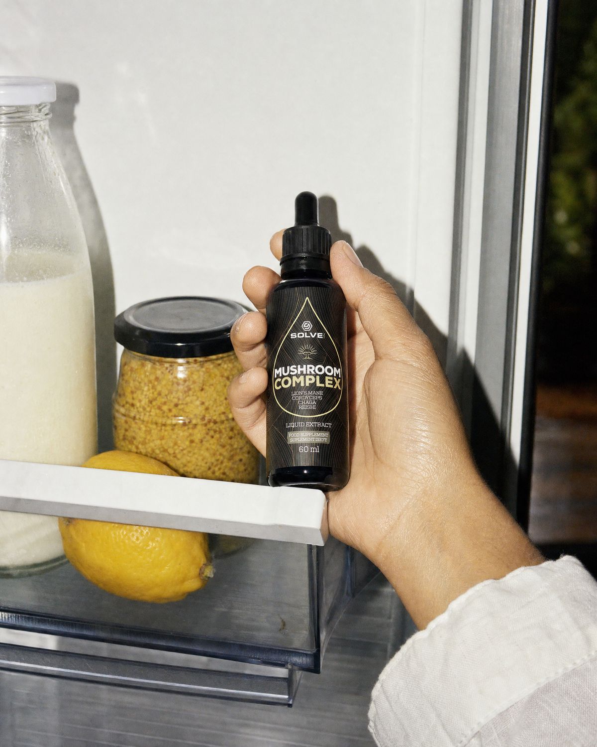 A hand taking the bottle of Solve Labs Mushroom Complex drops from a fridge door