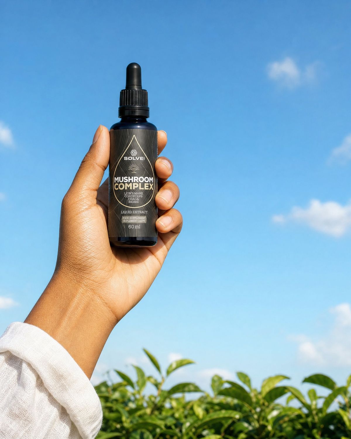 A hand holding up a bottle of Solve Labs Mushroom Complex drops against a blue summer sky