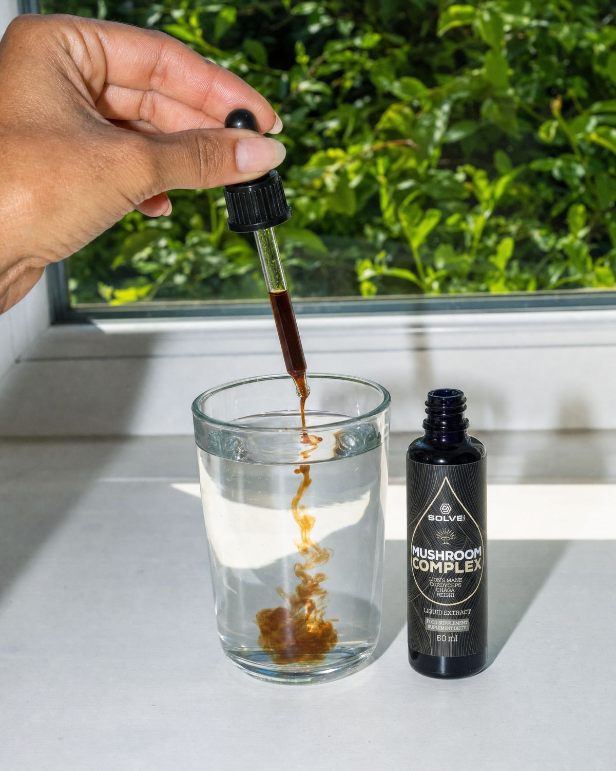 A dropper of Mushroom Complex liquid extract over a glass of water beside the bottle