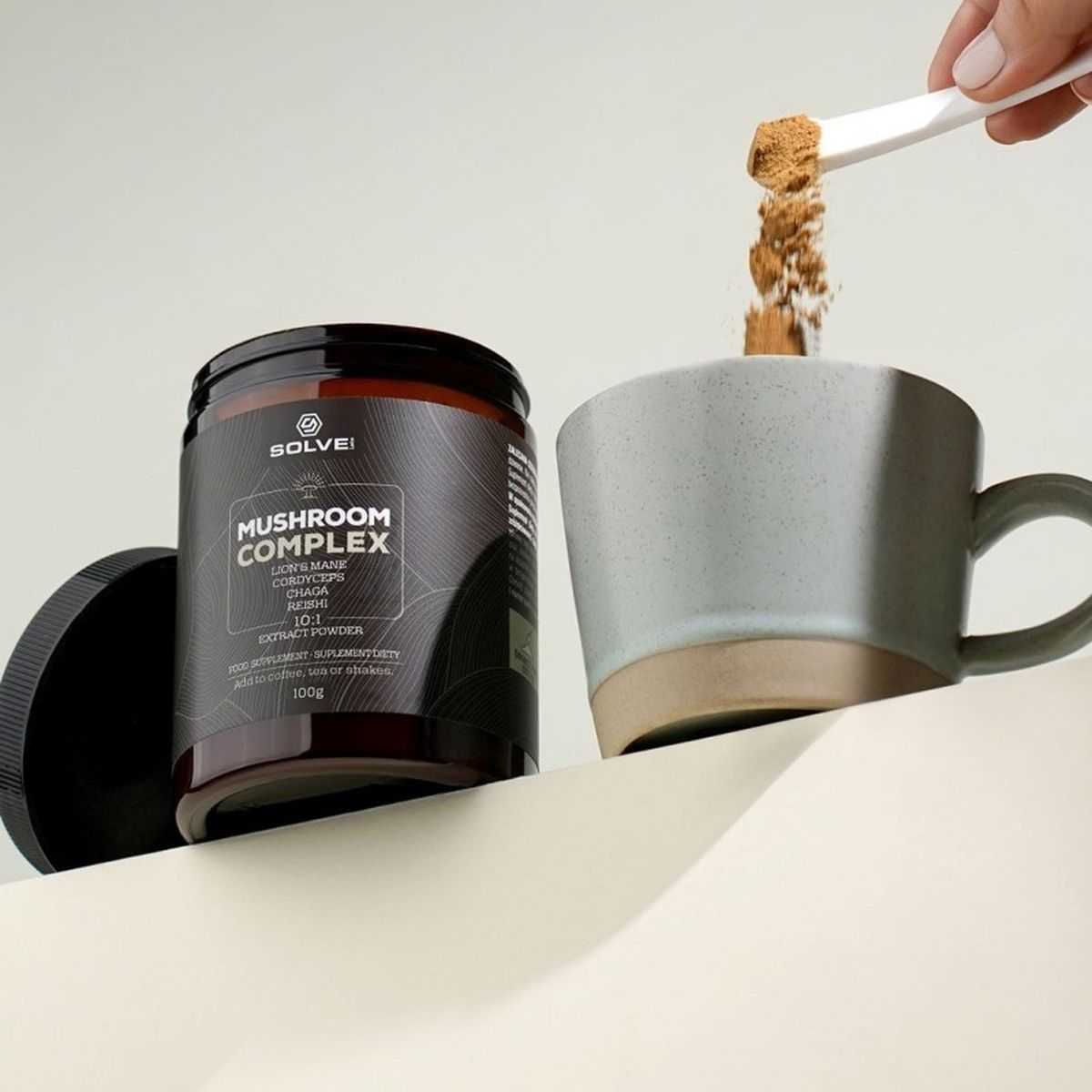 A scoop of Mushroom Complex powder falling into a stoneware mug beside the jar