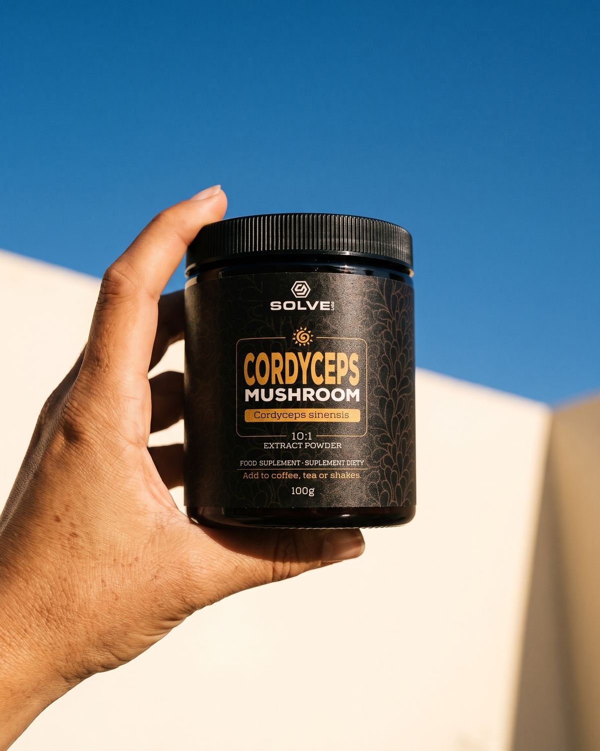 A hand holding up a jar of Solve Labs Cordyceps powder against a deep blue sky
