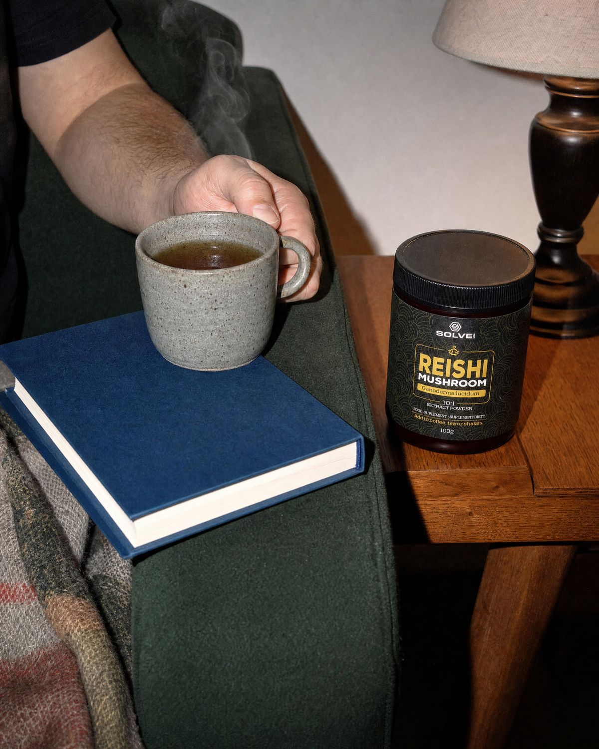 A mug of herbal tea on the arm of a sofa beside a book, the jar of Solve Labs Reishi on a side table