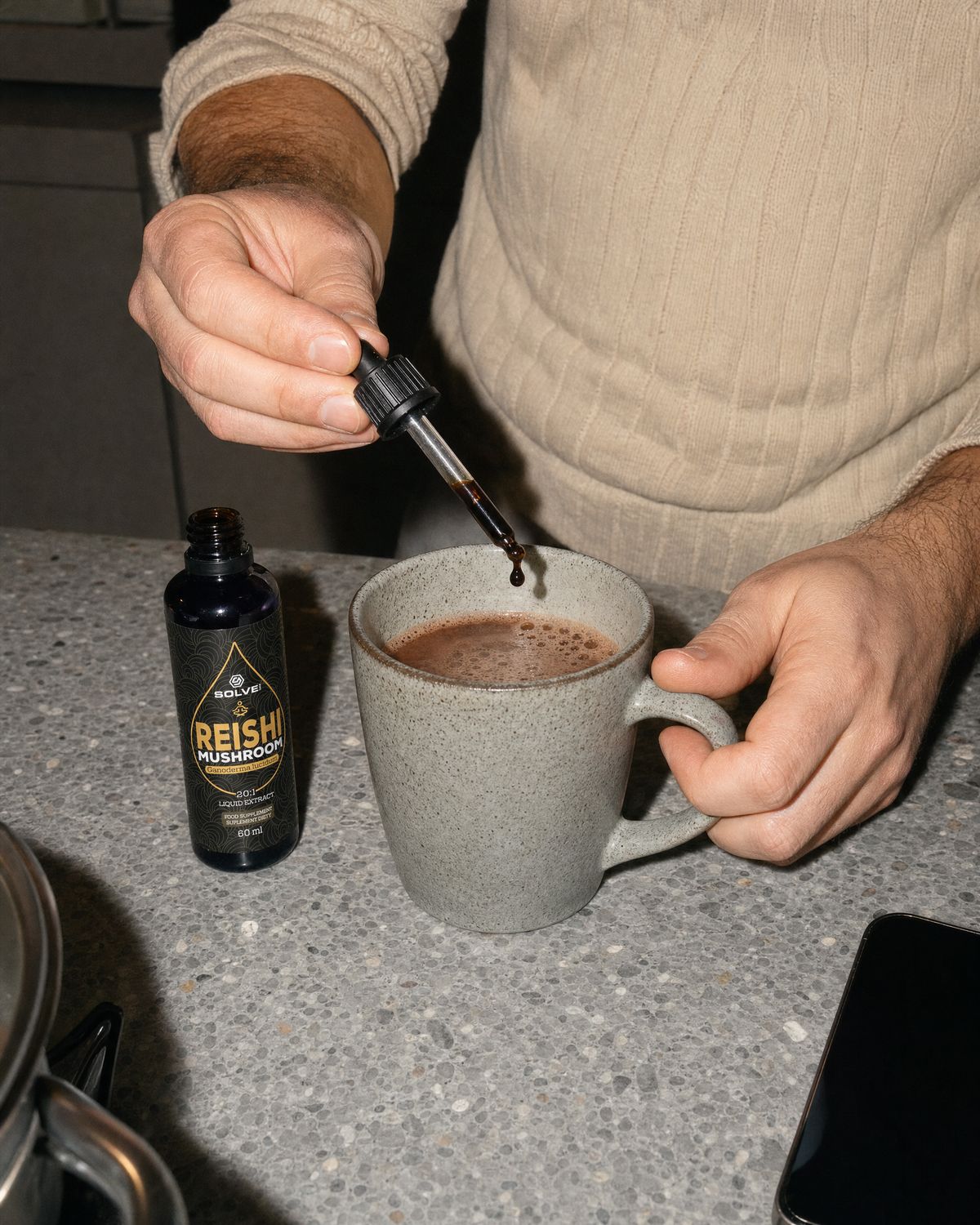 A dropper of reishi liquid extract over a mug of cacao beside the open bottle
