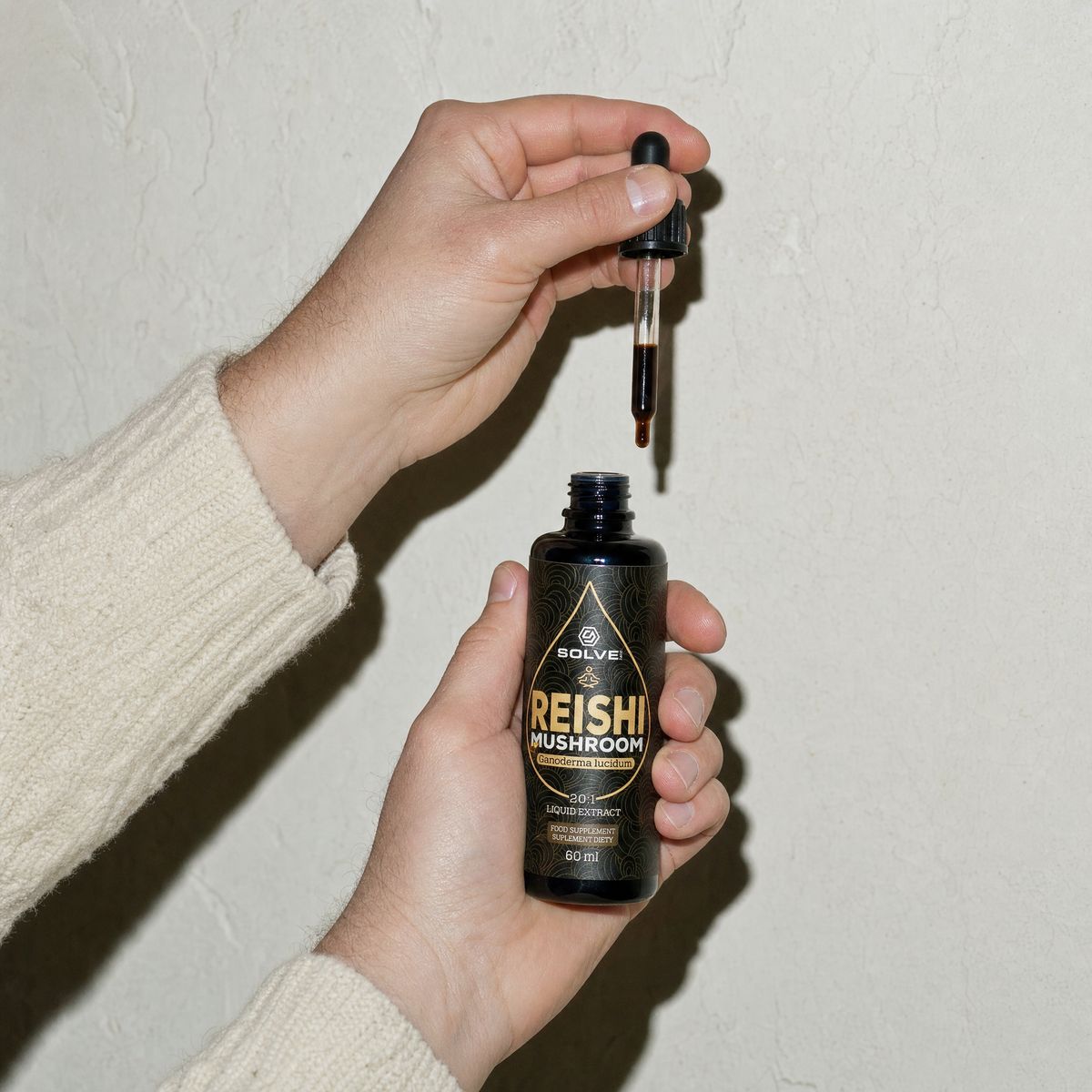 A hand holding a full dropper above the open bottle of reishi drops