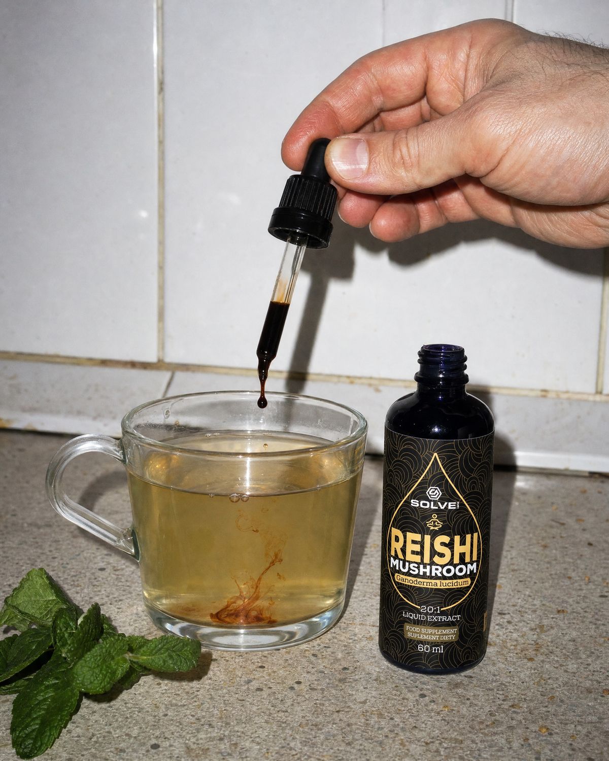 A dropper of reishi liquid extract over a glass of herbal tea beside the bottle