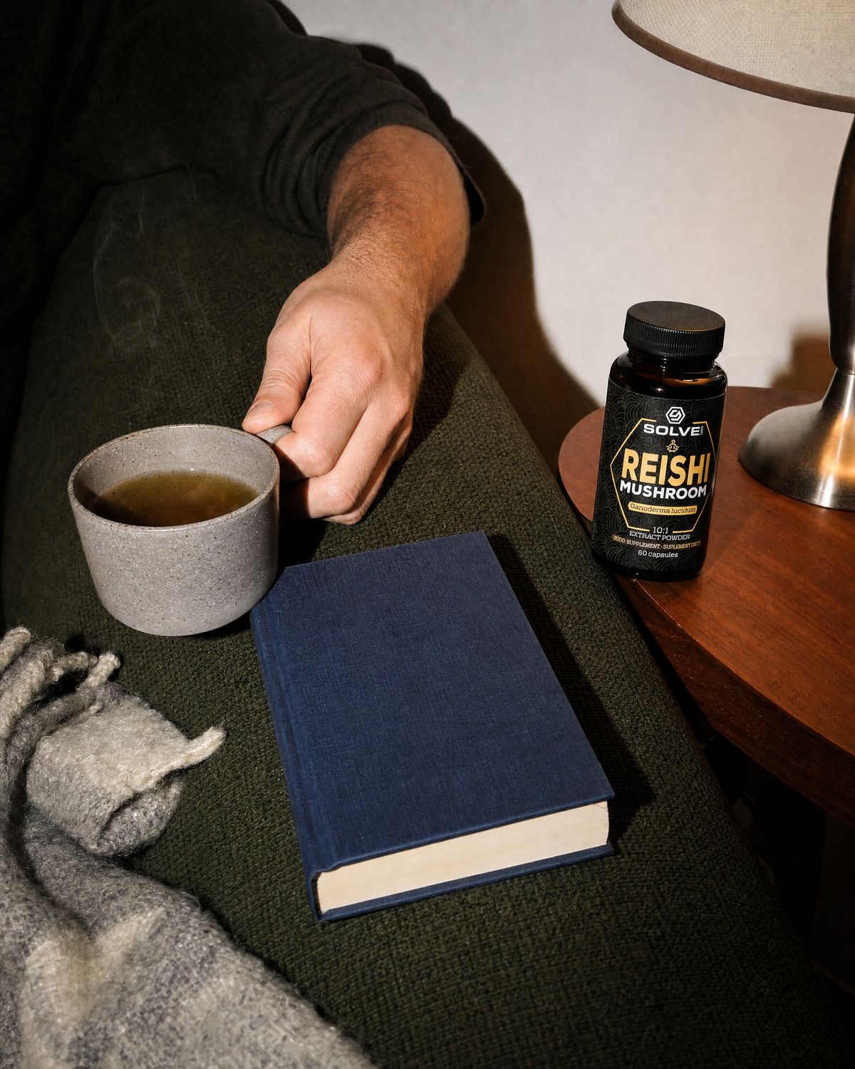 A mug of herbal tea on the arm of a sofa beside a book, the jar of Solve Labs Reishi capsules on a side table
