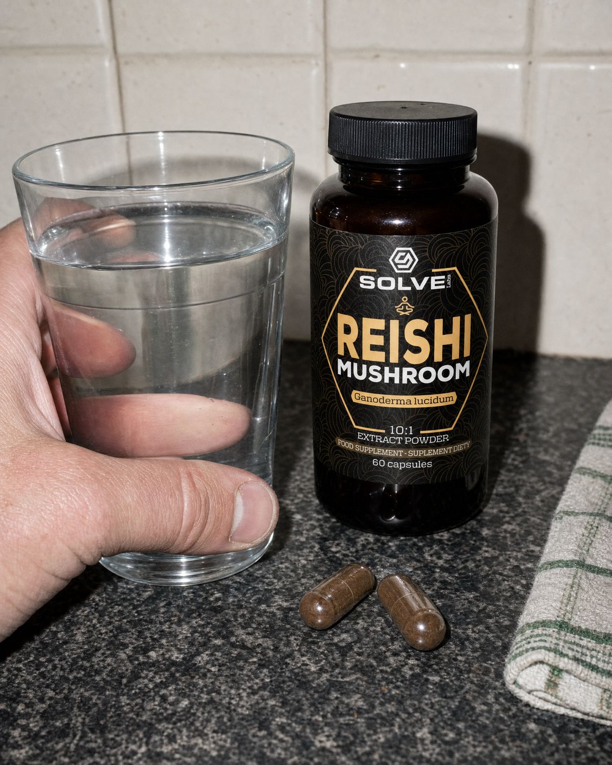 Two reishi capsules on a kitchen counter beside a glass of water and the jar