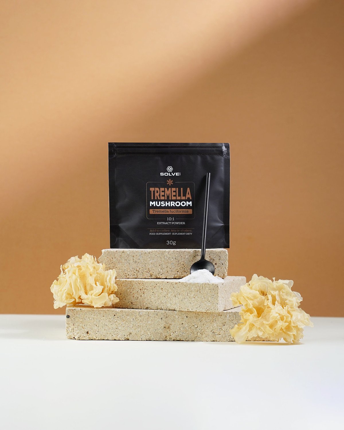 Der Beutel Solve Labs Tremella-Pulver auf hellen Steinplatten mit einem Löffel des Pulvers und getrocknetem Schneepilz