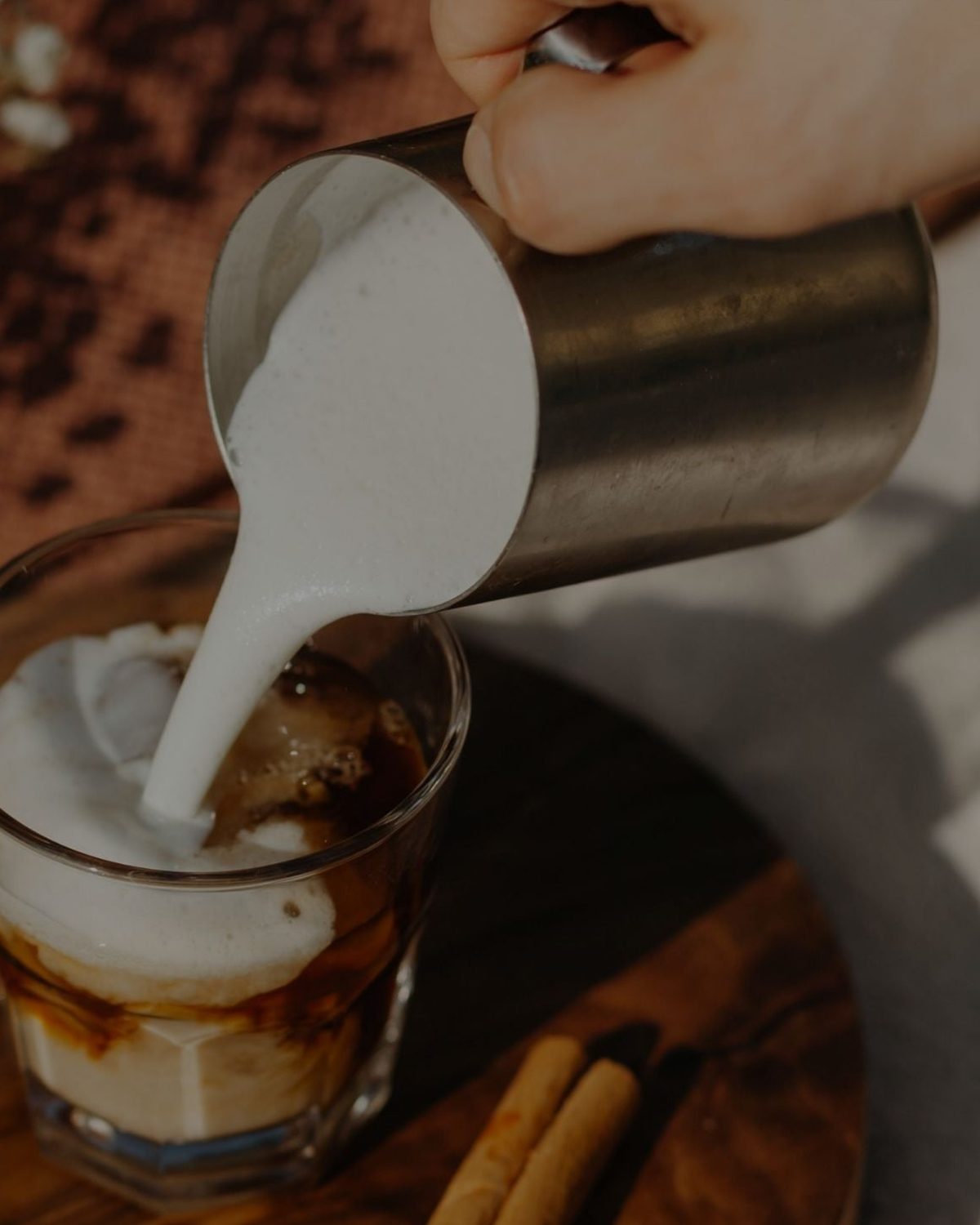 Hot milk being poured into a glass of Mushroom Cacao on a wooden board with cinnamon