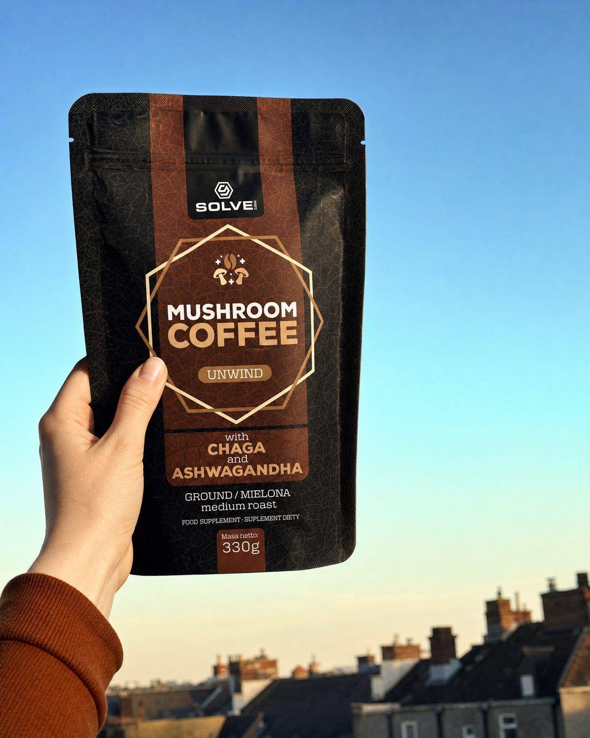 A hand holding up a bag of Solve Labs Mushroom Coffee with Chaga against an afternoon sky