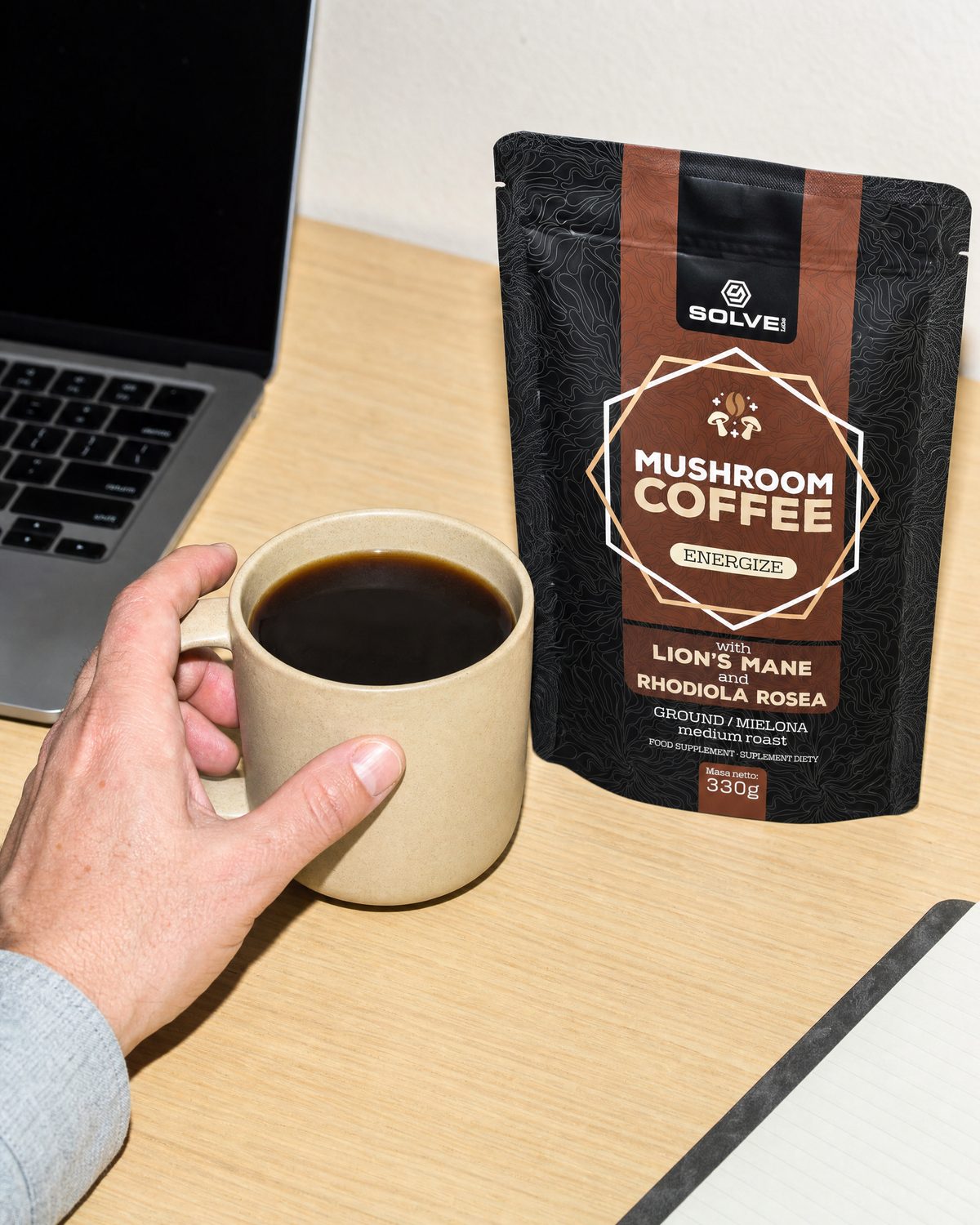 A hand lifting a stoneware cup of coffee beside a bag of Mushroom Coffee with Lion&rsquo;s Mane