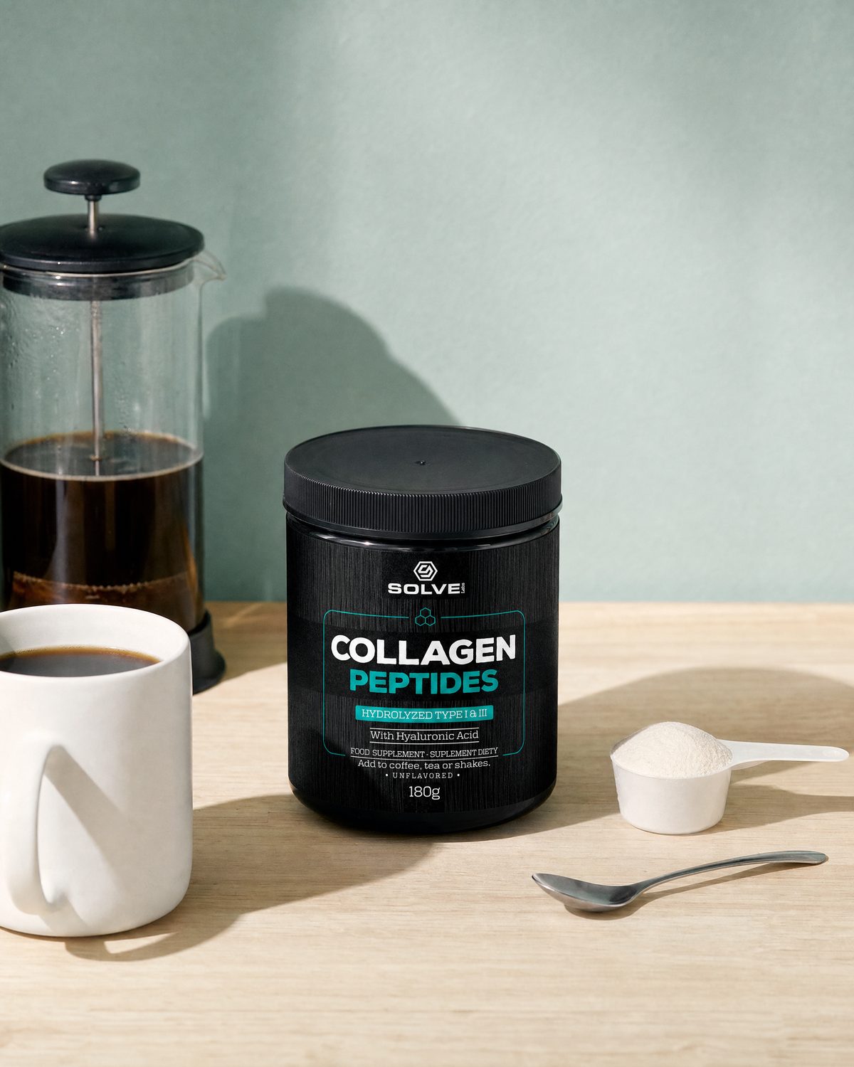 The tub of Solve Labs Collagen Peptides on a breakfast table with a cafetière, a mug of coffee and a scoop of the powder