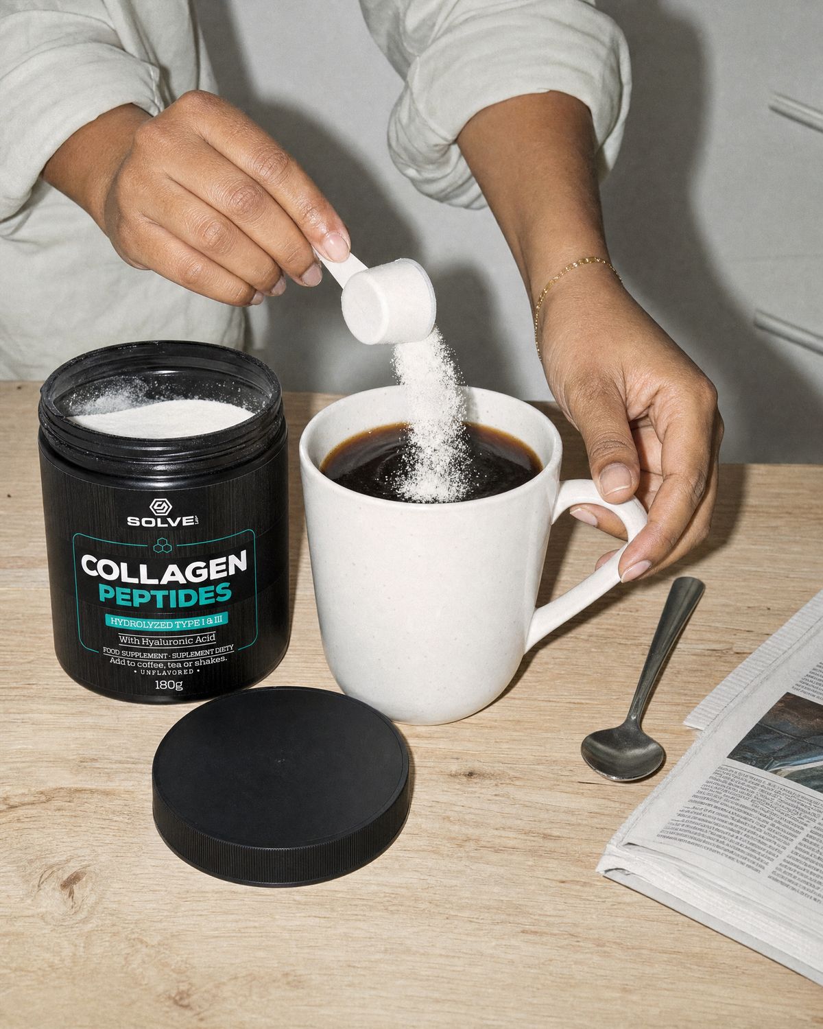 A scoop of white collagen powder falling into a mug of black coffee beside the open tub
