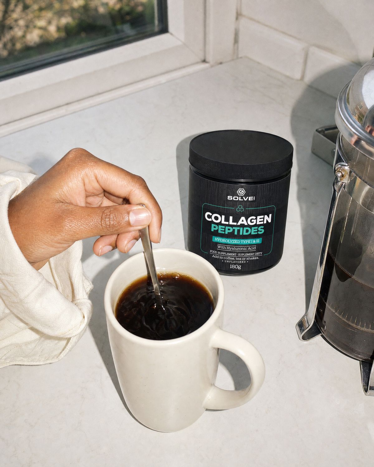 A hand stirring a mug of black coffee beside the tub