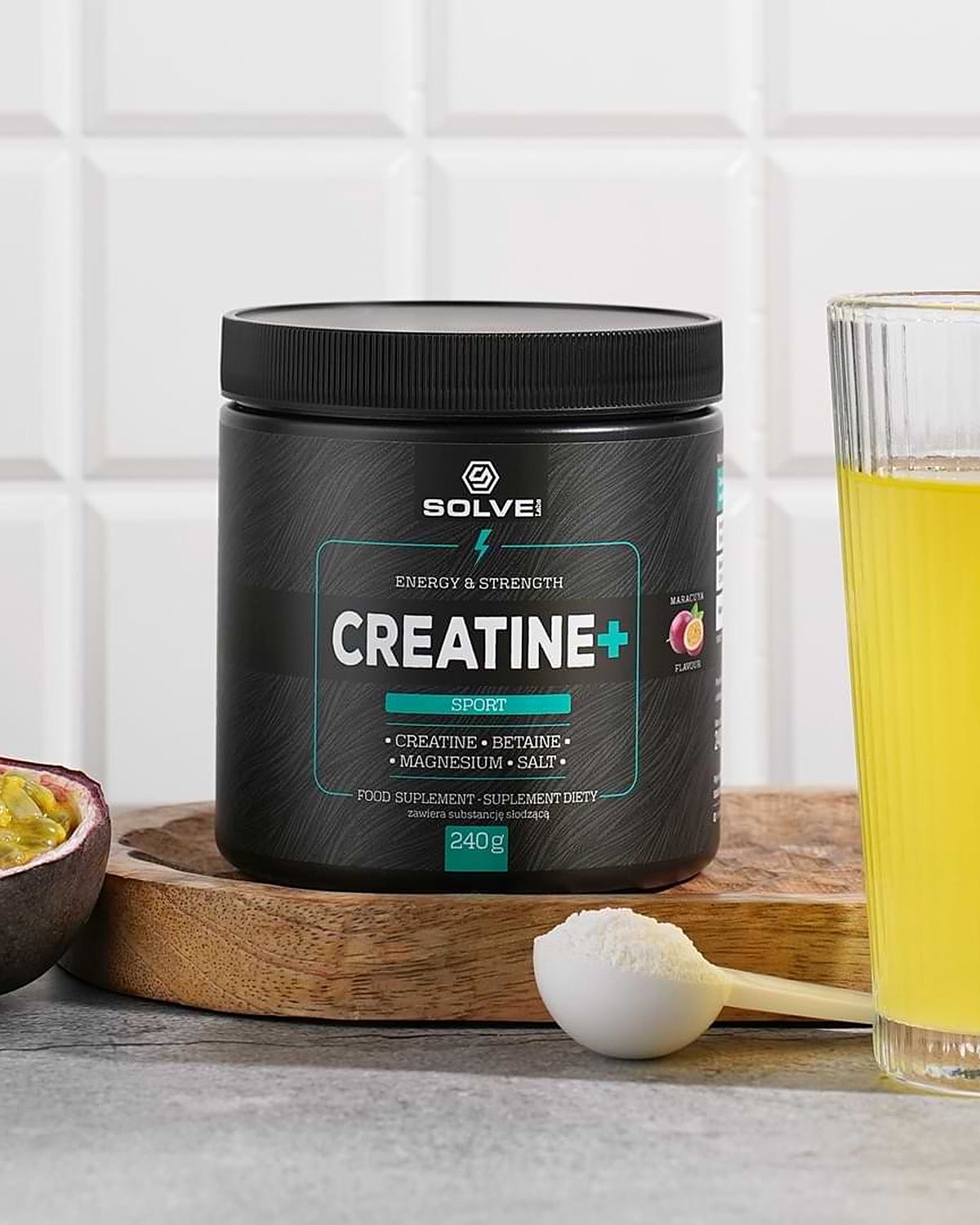 The tub of Solve Labs Creatine+ on a wooden board with a halved passion fruit and a glass of the drink