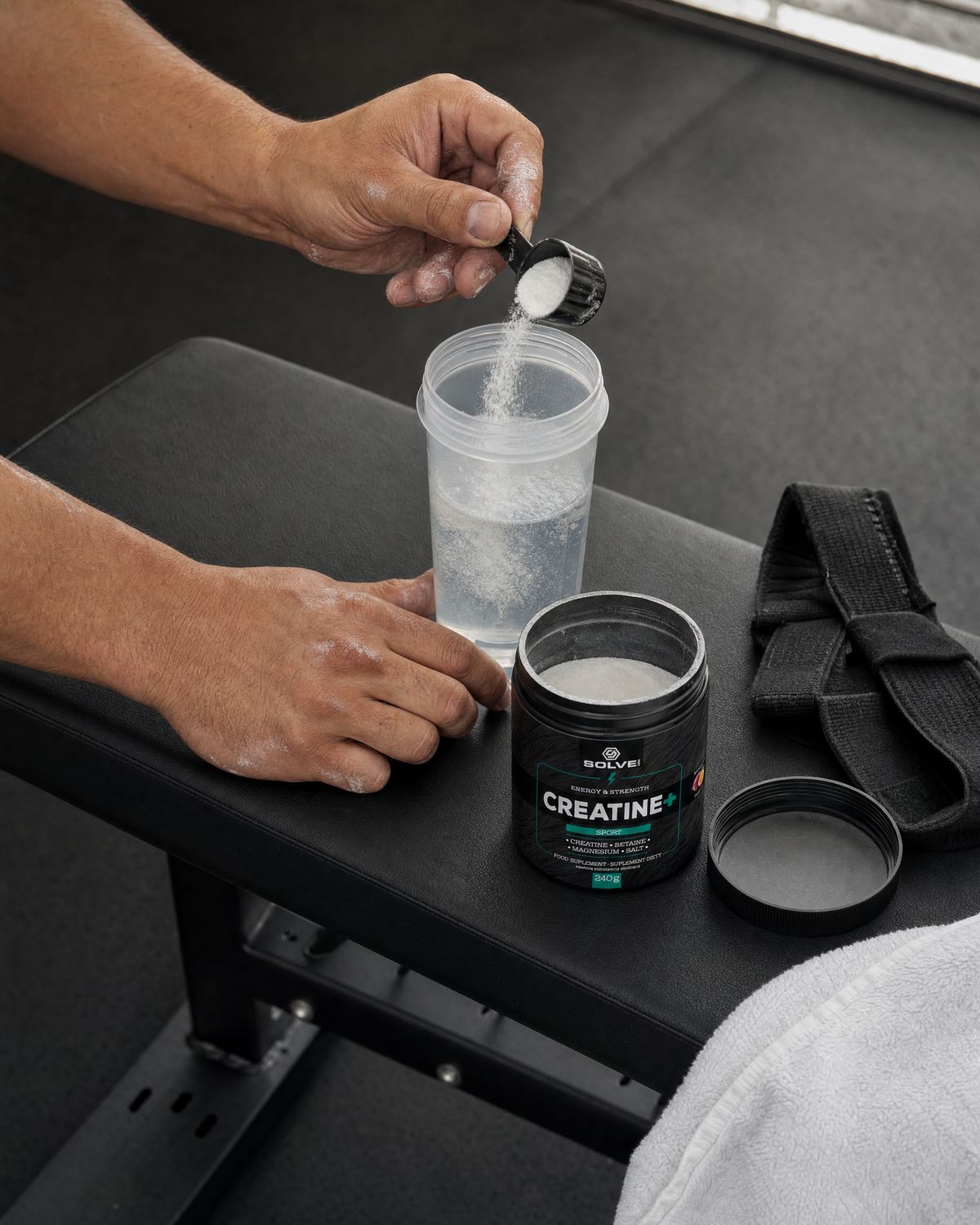 A scoop of white creatine powder falling into a shaker of water beside the open tub